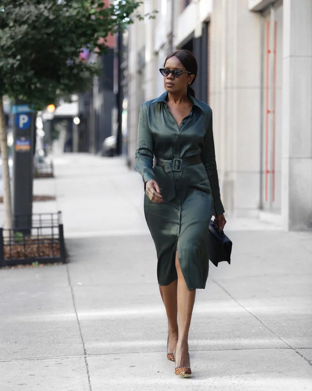 Elaine Davis wearing a dark green belted shirt dress with an open collar, neutral pointed heels and a small dark clutch.