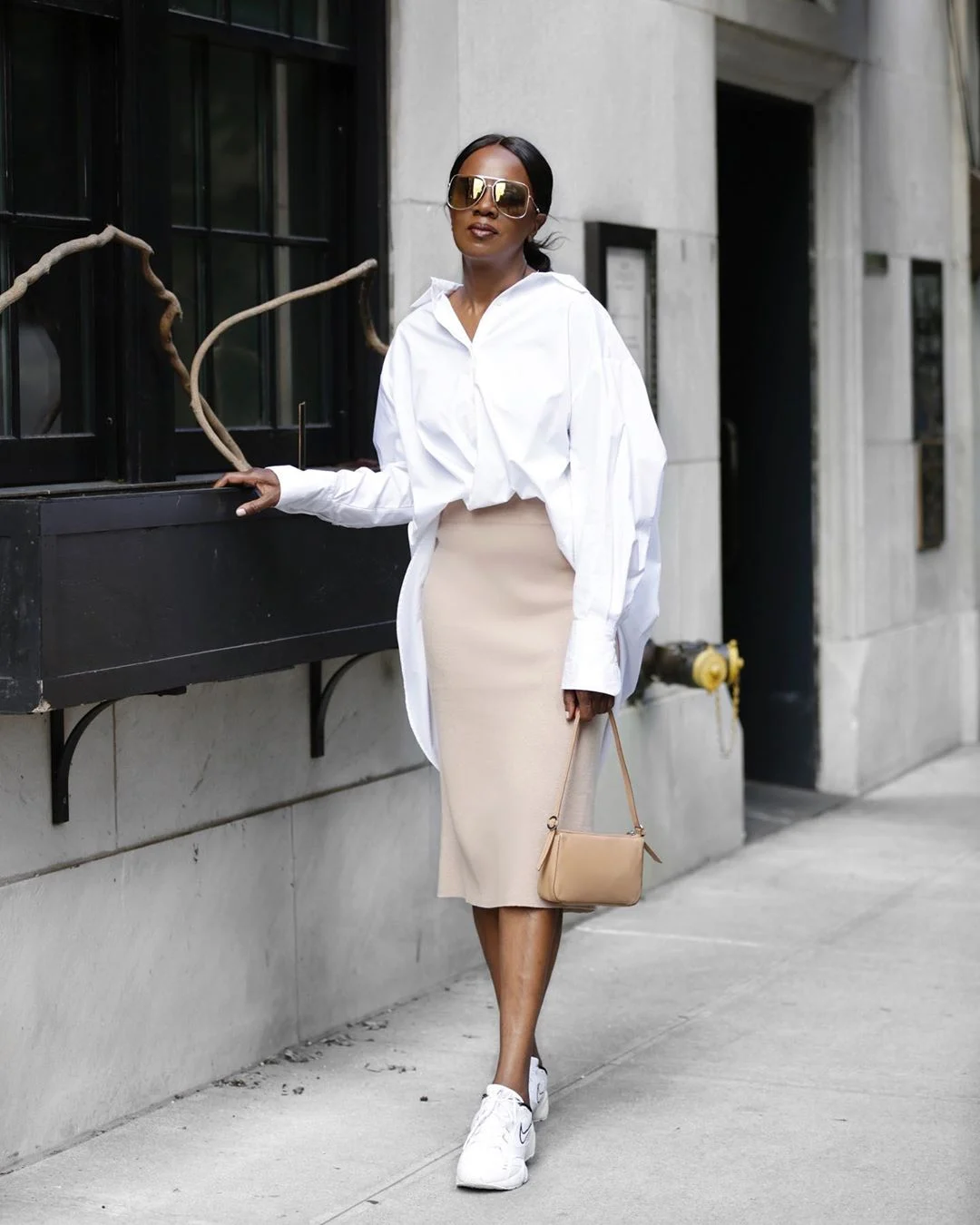 Elaine Davis wearing a loose white shirt, beige midi pencil skirt, white sneakers and a small beige bag.