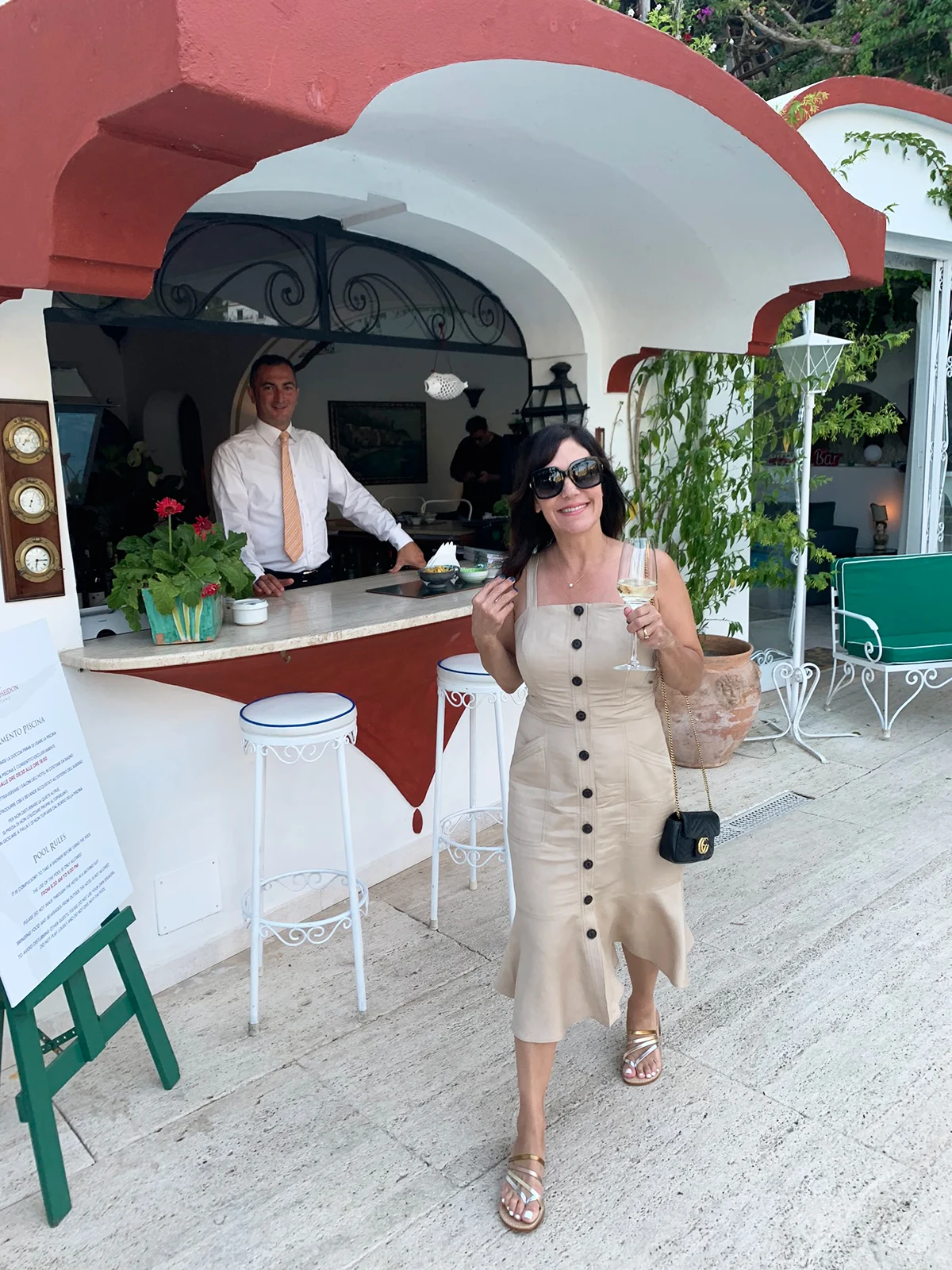 Susie Wright wearing a beige sleeveless button-front midi dress with flat patterned sandals and a small dark crossbody bag.