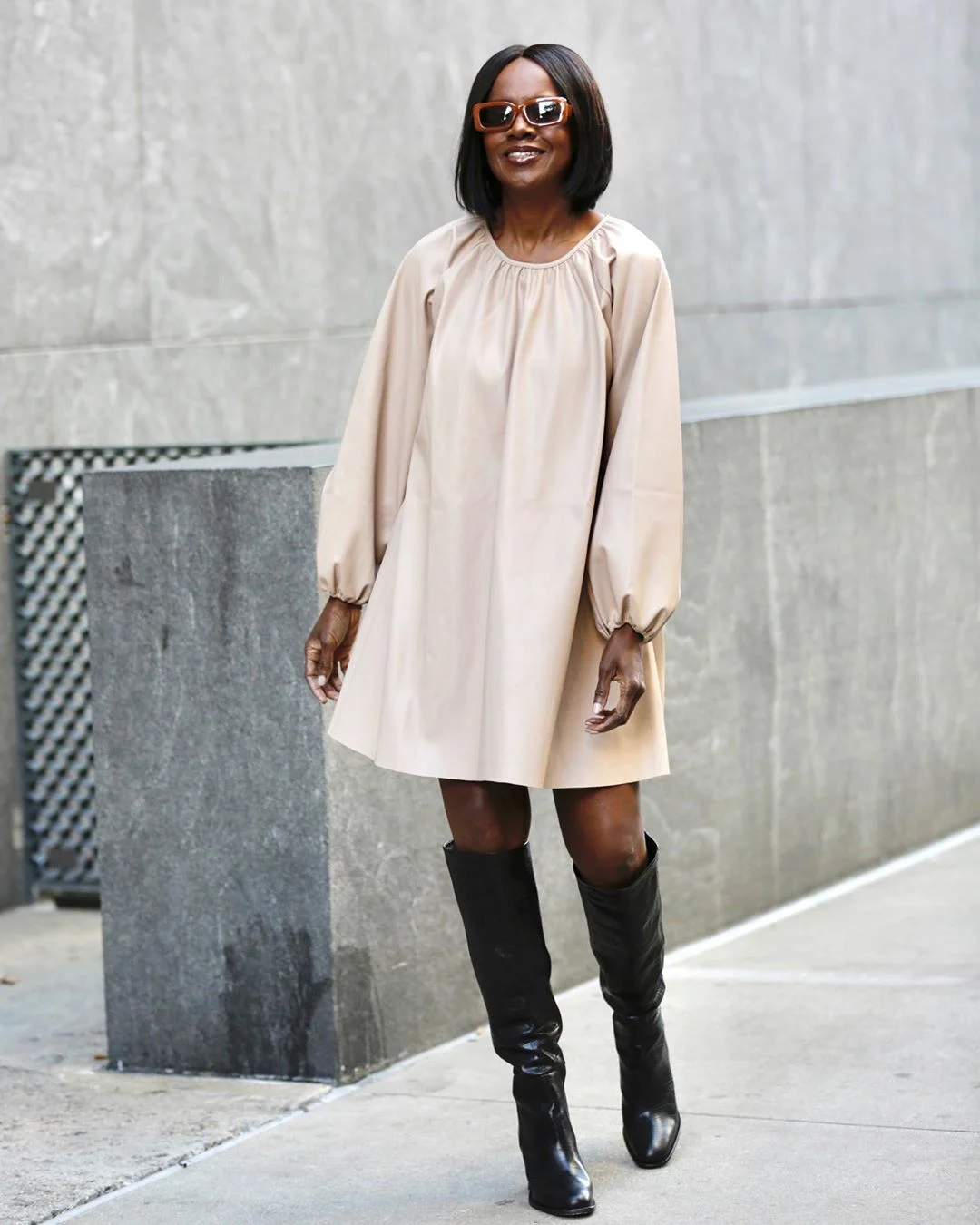 Elaine Davis wearing a loose long-sleeved beige dress above the knee with tall black boots.